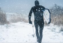 man carrying surfboard walking on snow