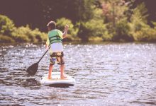 Young boy in a life vest paddleboarding on a lake.